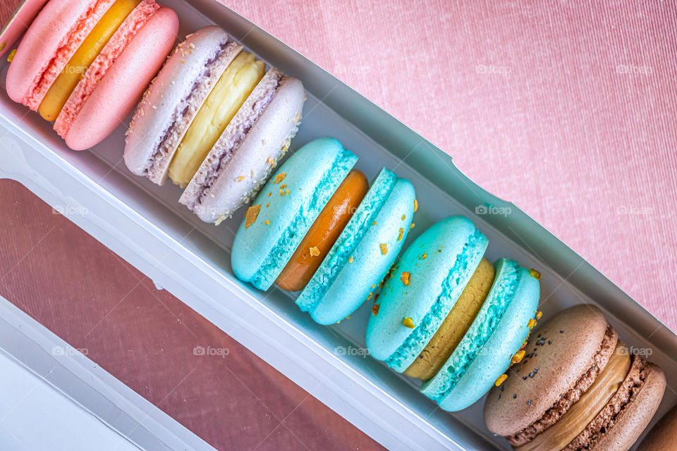 Top view of open box with assorted macarons filled with cream.