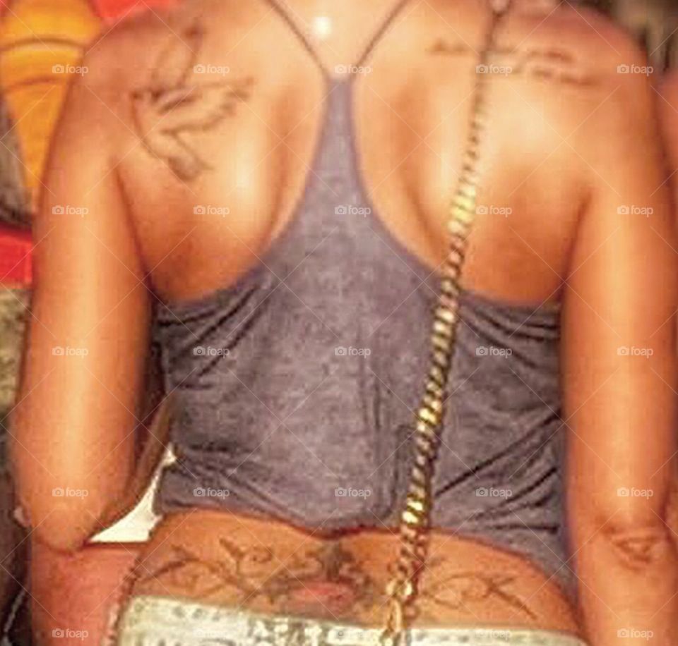Back of young sexy female outdoors in tank top with tattoos and gold shiny strap of a purse.