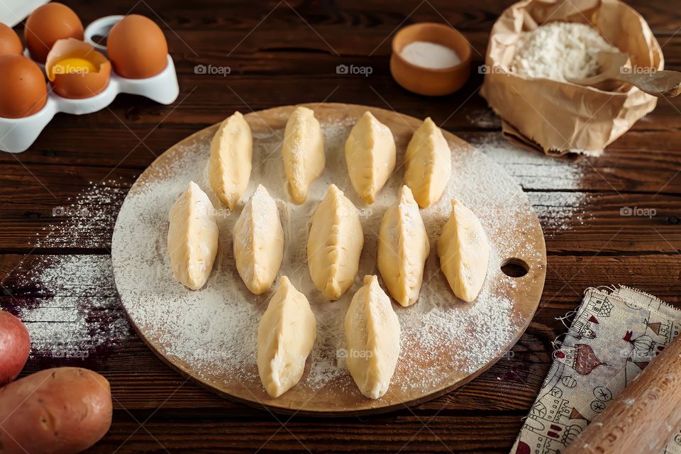 Close up Russian pirozhki baked patties ready to be baked surrounded with eggs, flour and other ingredients.