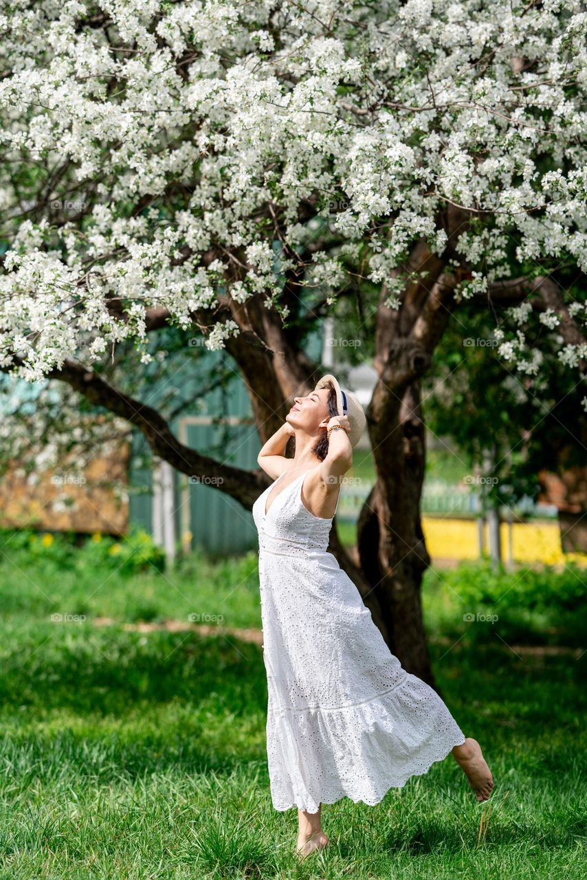 Woman in white dress enjoying sunny weather. Blooming apple tree. Spring season