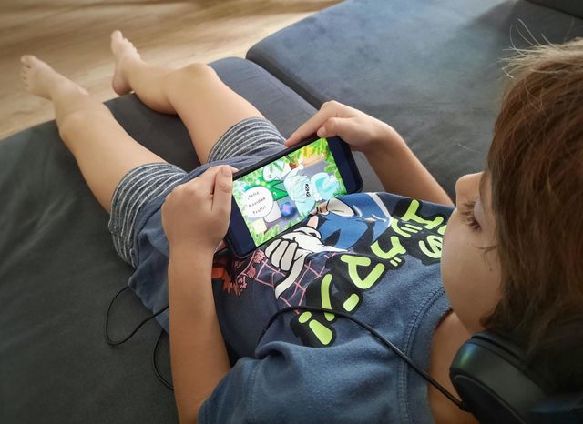 Perspective shot of my 7 year old son on the couch playing a video game on his smartphone with his headphones.