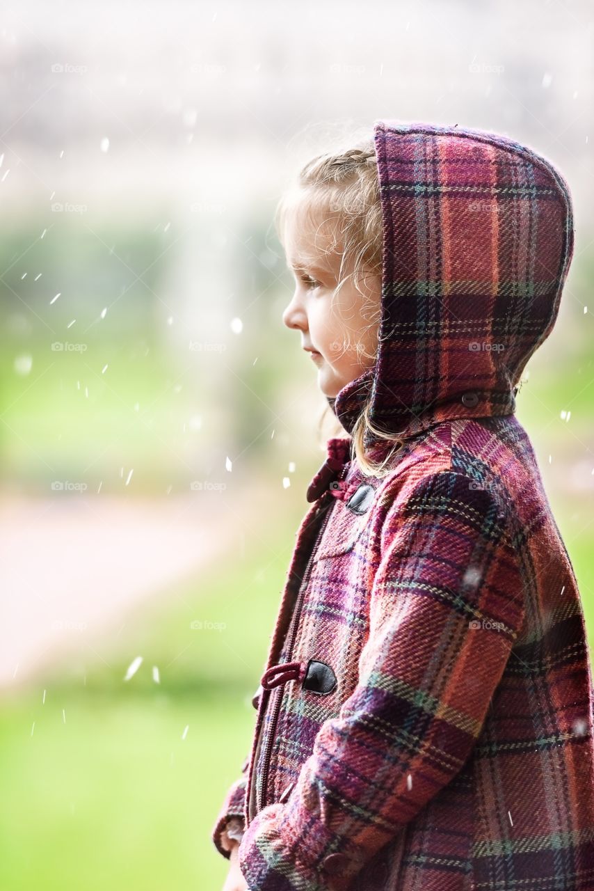 Little girl in a plaid coat in the rain in the park