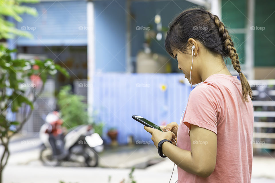 Hand of a woman wearing a watch and holding the phone plugged in headphones.