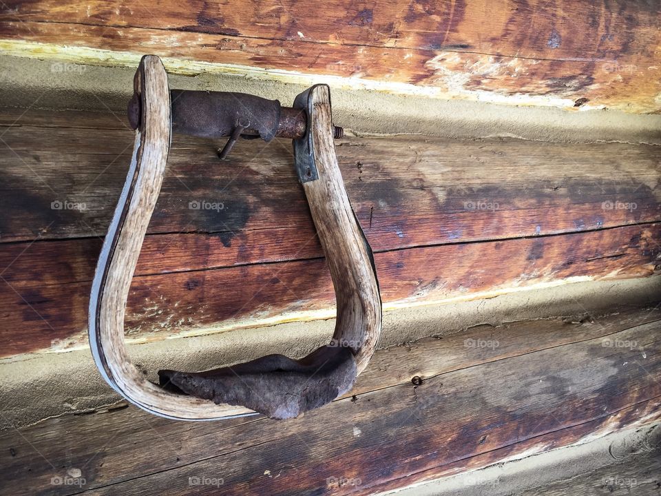 Antique saddle stirrup hanging on the wall of an old log cabin
