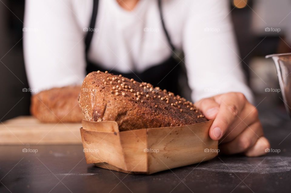 Freshly home baked, wholegrain, rye, brown loaf of bread in wooden baking tray on kitchen work top.