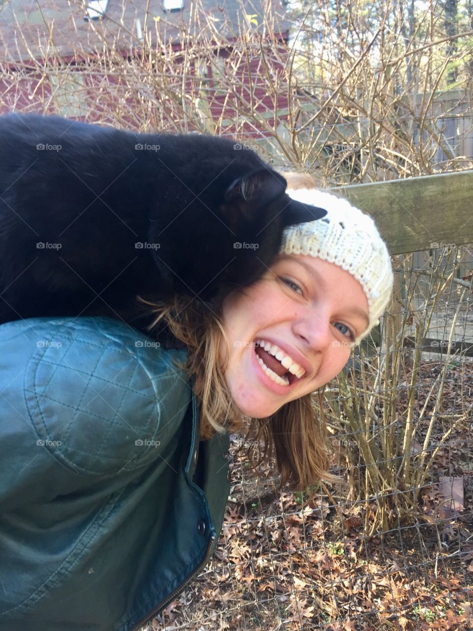 A young woman in a white headband smiles while holding a black cat