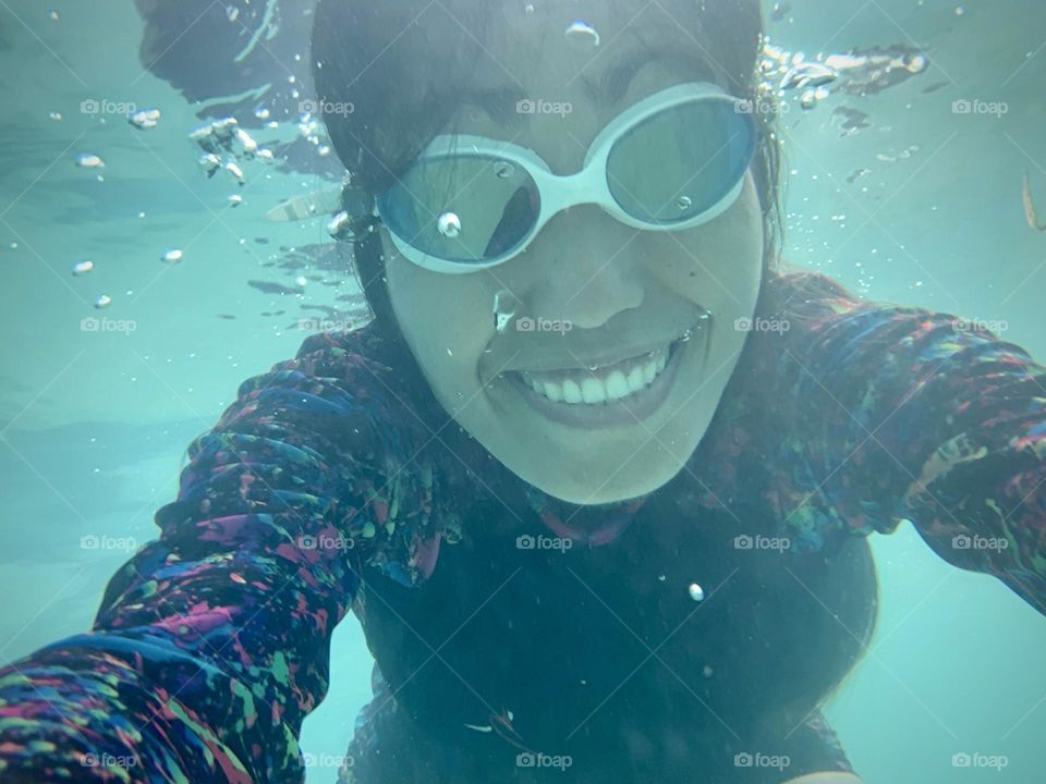 Portrait of young adult woman wearing goggles and with smile on her face while under water. 