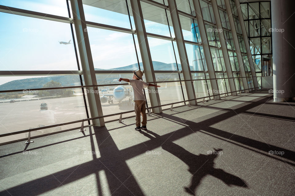 A boy in an airport standing near the window and looking at departuring plane.