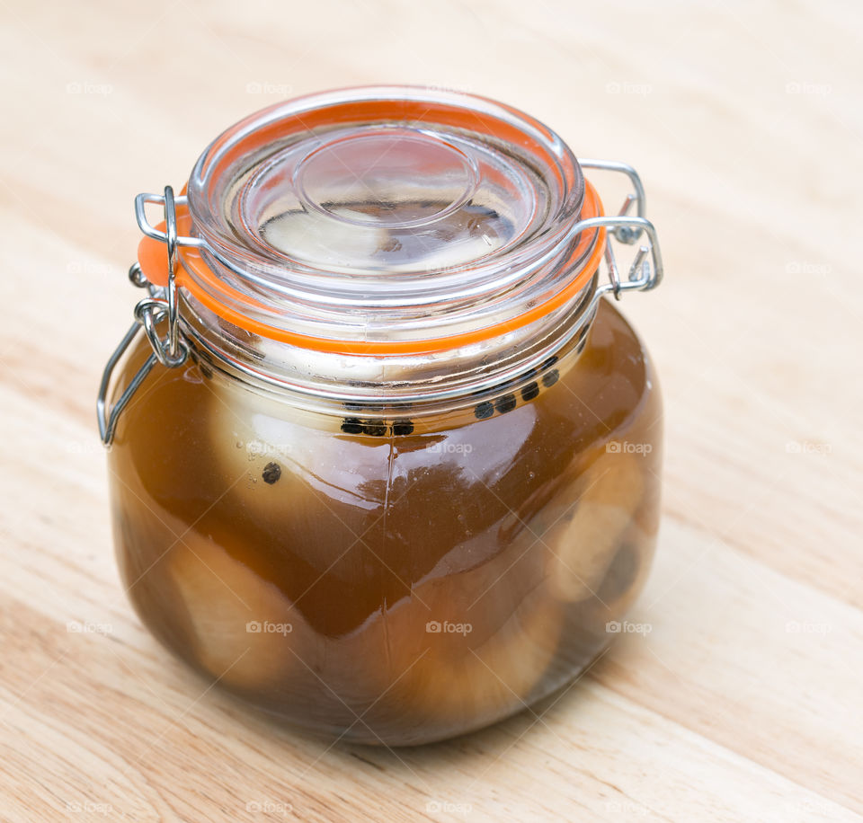 One jar of homemade pickled onions with the lid clamped down on a wooden background.