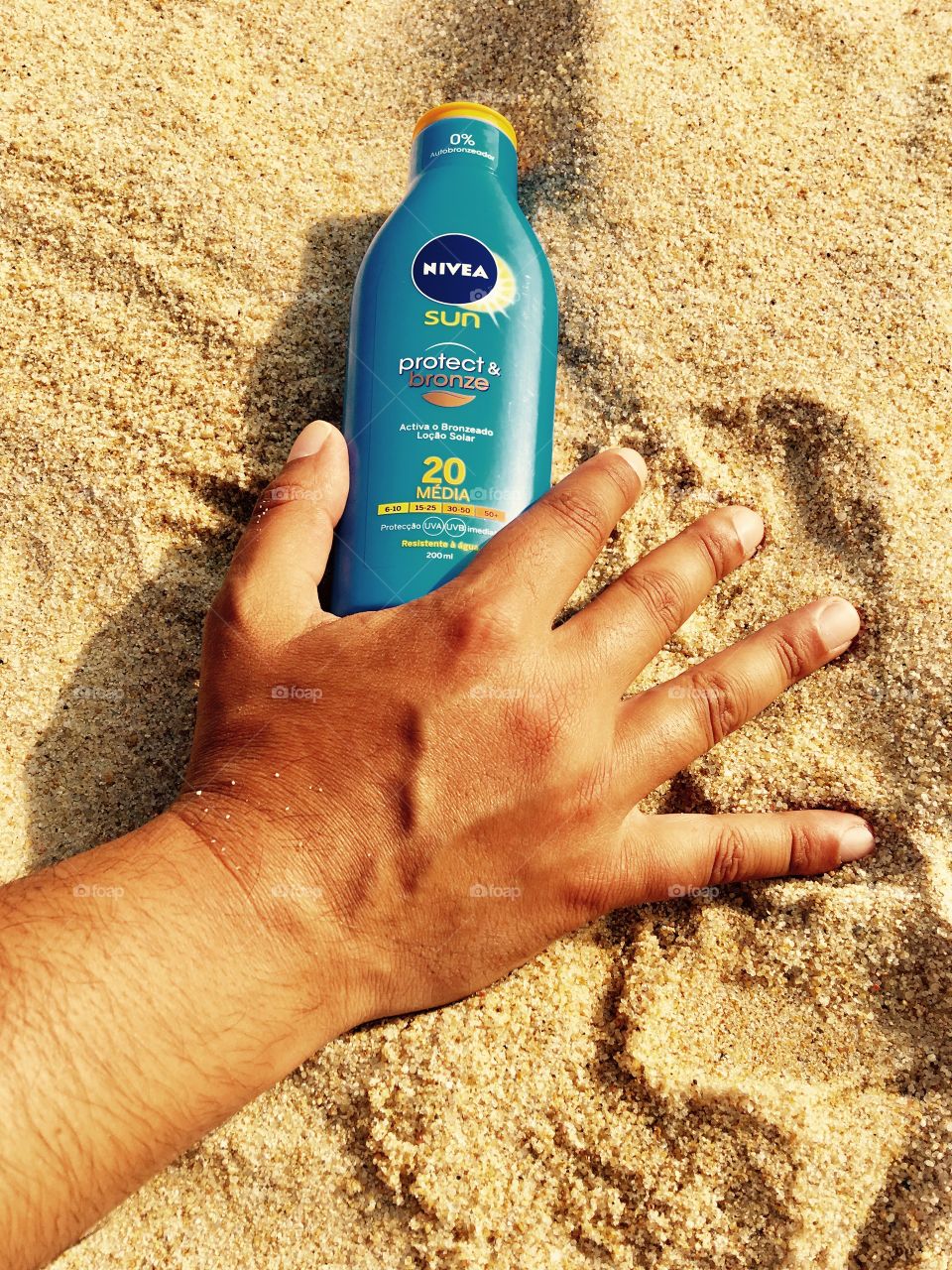 Hand holding bottle of Nivea Sunscreen Protector in the beach’s sand 