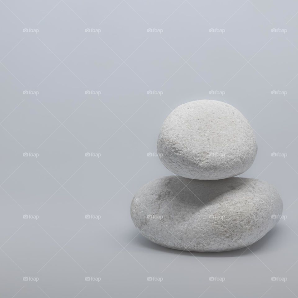 Two white pebbles, one balanced on top of the other, against a pale grey background 