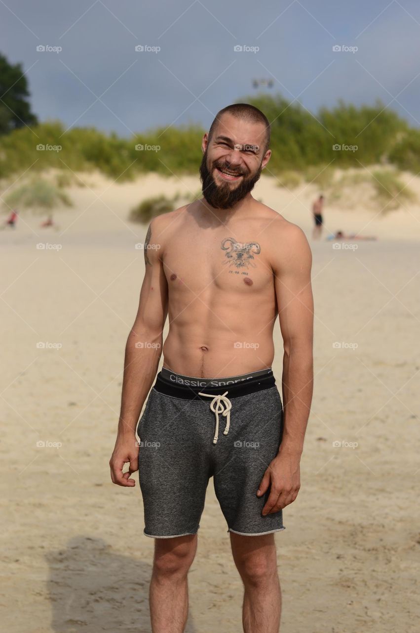 man with beard and tattoo shirtless on the beach