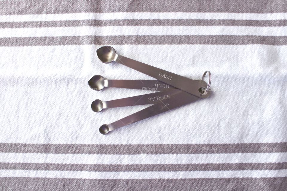 Overhead view of miniature stainless steel measuring spoons on a white-and-grey-striped dish towel