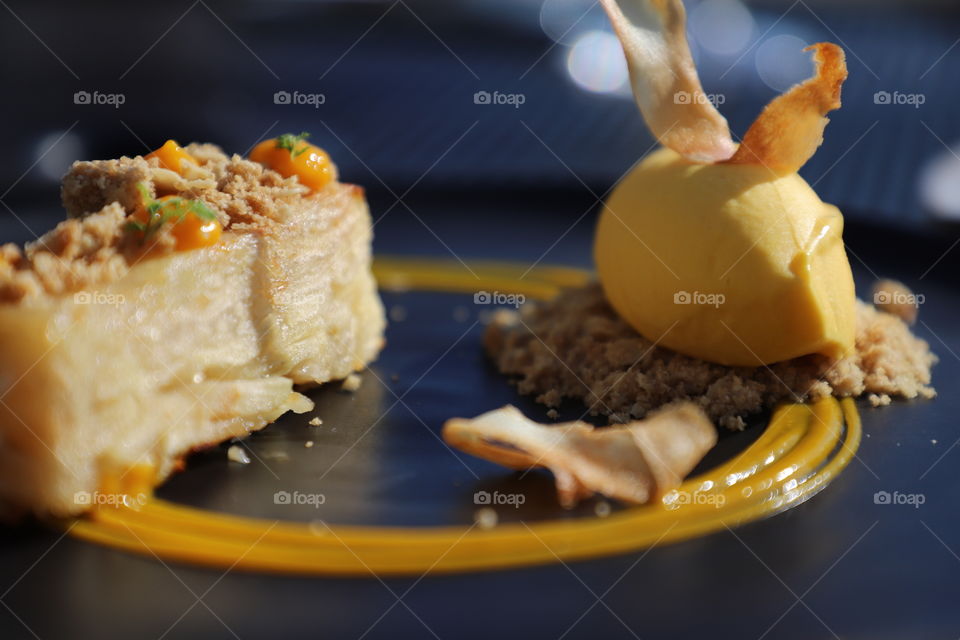 Apple crumbles and mango sorbet on top of black fancy plate decorated with yellow paste 