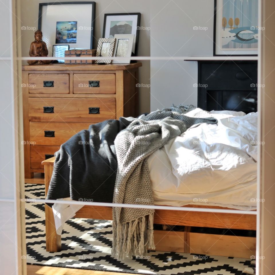 Unmade bed in reflection. Grey bedroom with wooden floor. 