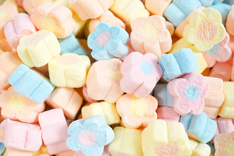 Marshmallows. A pile of cute flower marshmallow, colorful food pattern. Can be used for food container advertising. Selective focus on the orange and blue flowers in the middle.
