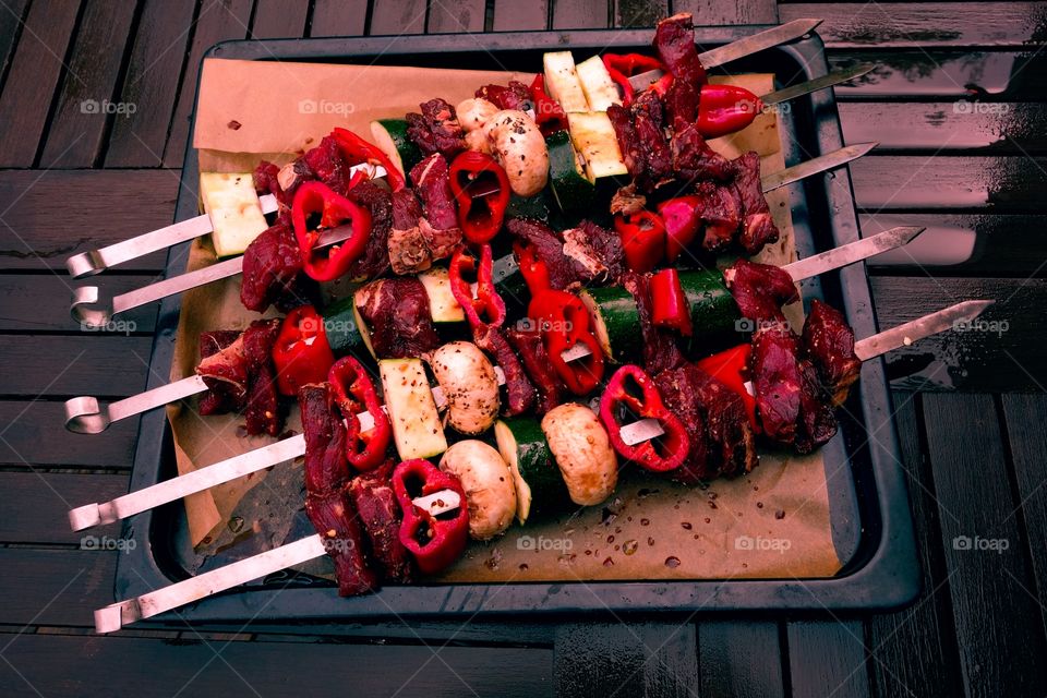 Shashlik skewers with meat. Caucasian shashlik skewers filled with raw meat and vegetables on an oven plate on a rainy summer day outdoors.