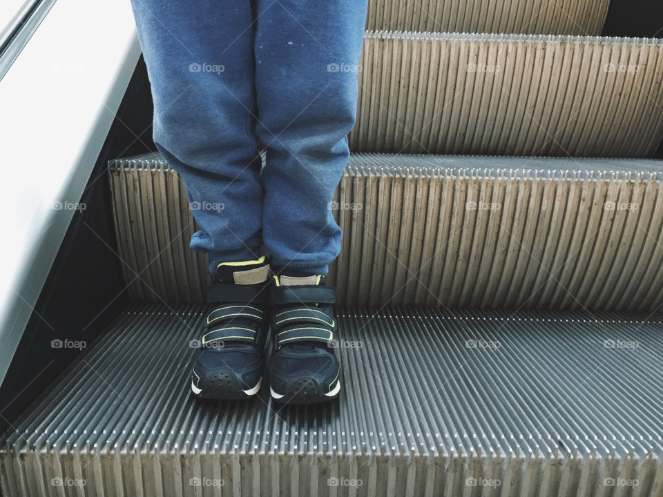 Boy on escalator, closeup. Boy in sneakers on escalator, closeup