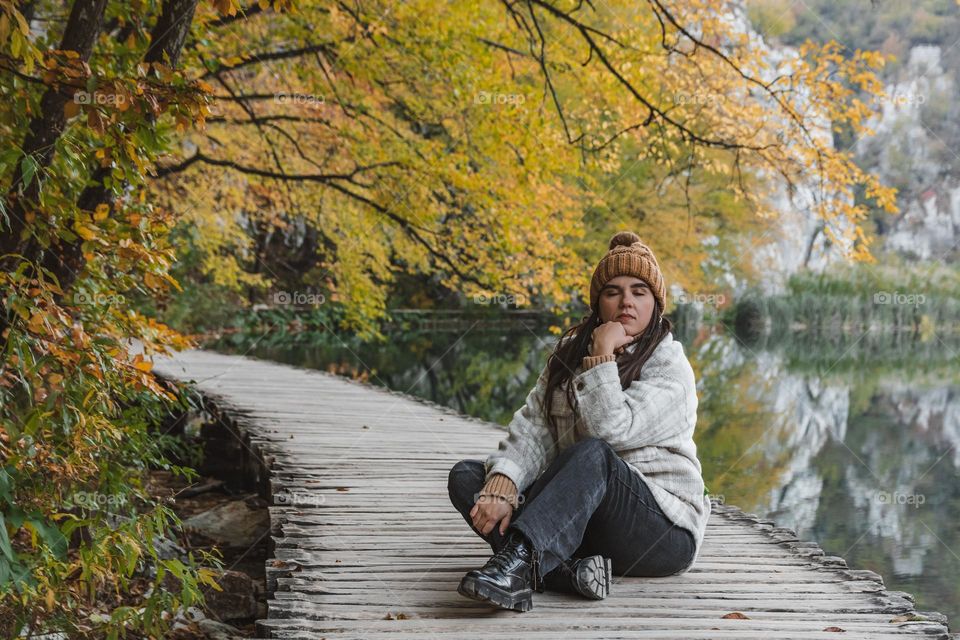 Girl sitting on wooden walkway under autumn trees by a lake