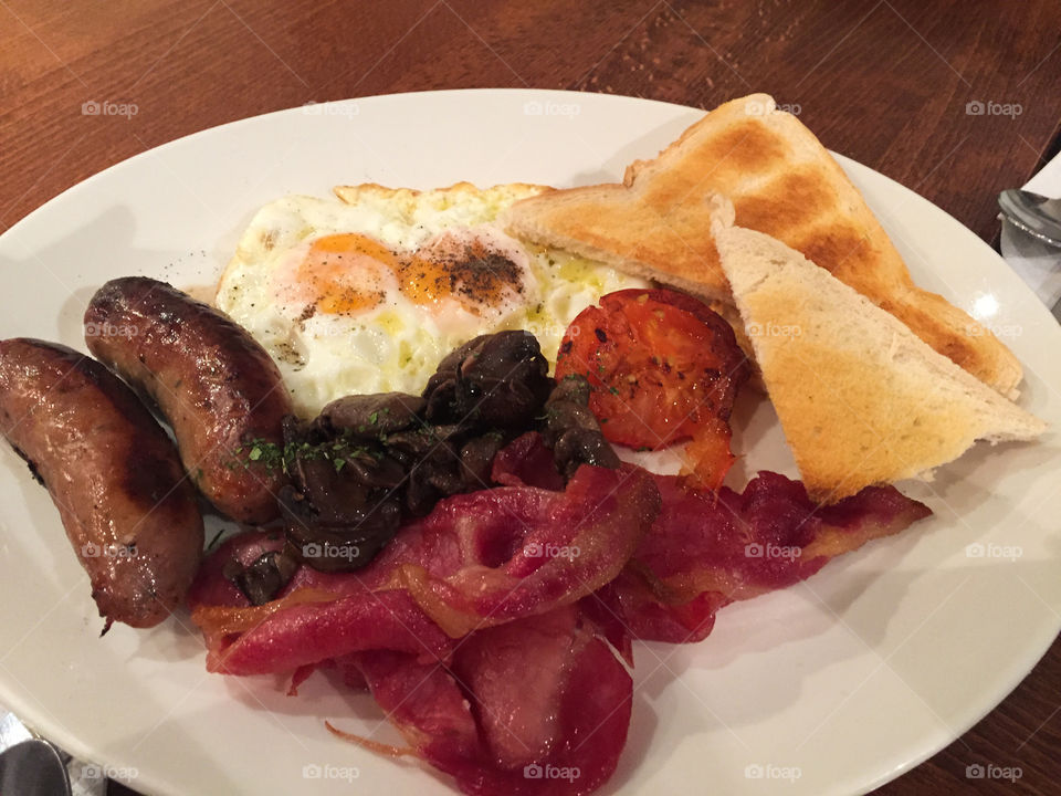 Traditionel english breakfast with sausage, bacon, eggs, mushrooms, tomato and toast