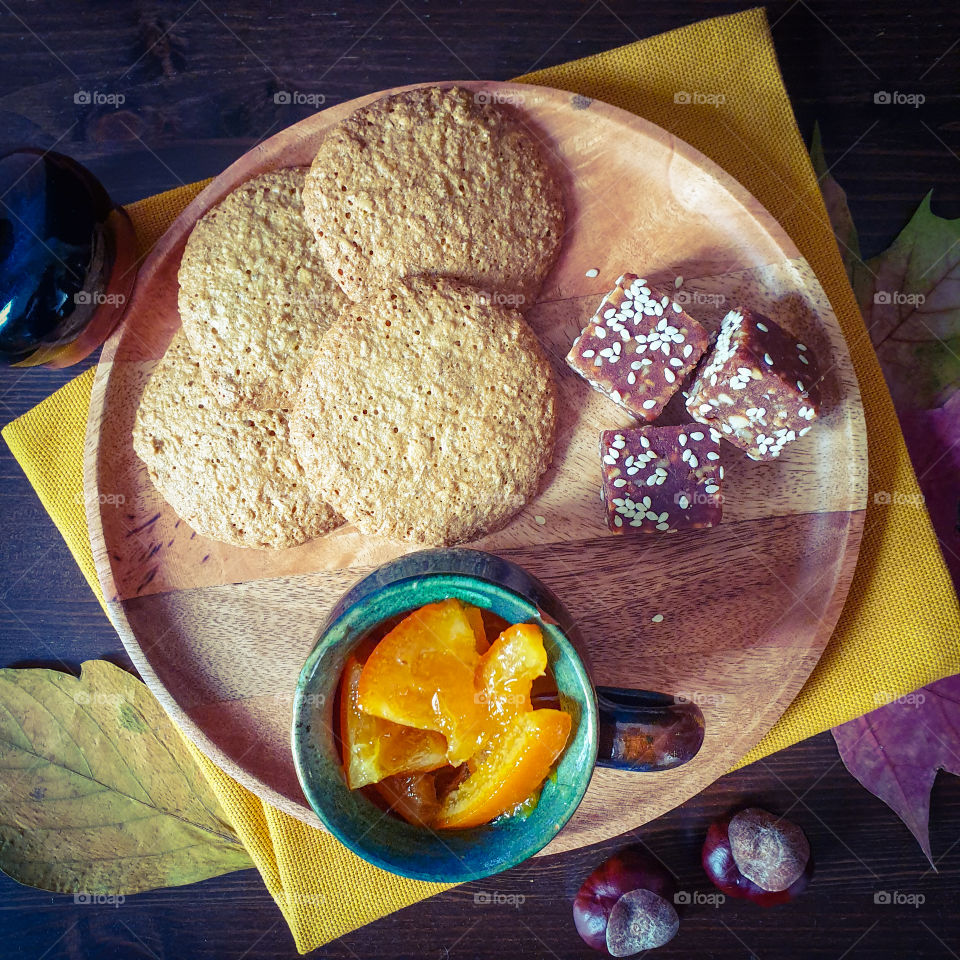 Autumn still life with homemade cakes.  Wooden tray with homemade biscuits, a clay pot with orange jam and sweets on a bright yellow napkin with dry leaves and chestnuts.  Autumn mood