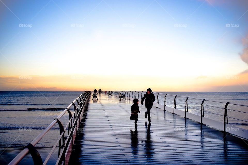 Children run on a wet wooden pier in winter.
