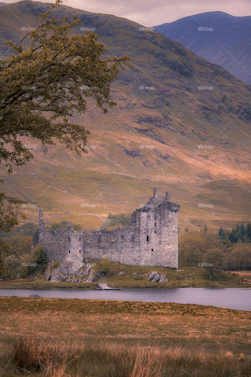 Old abandoned castle in the highlands of Scotland. Moody mountain scene with soft green tones as the sun tries to break through the clouds. 