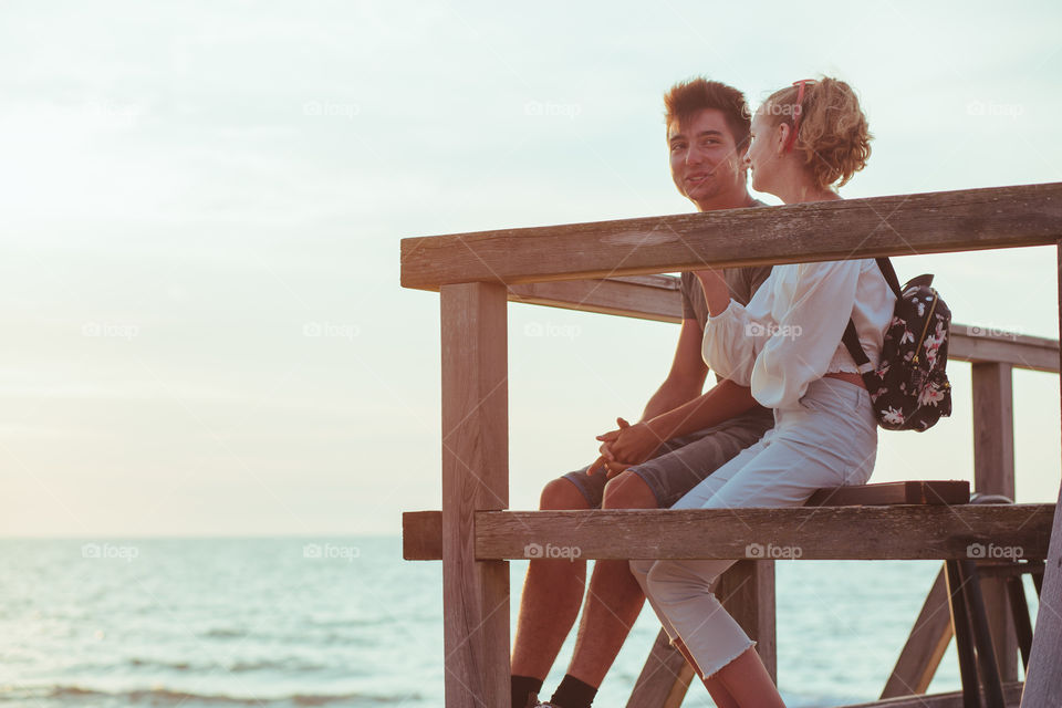 Happy smiling couple of young woman and man sitting on a pier over the sea during summer vacations. Copy space room for text