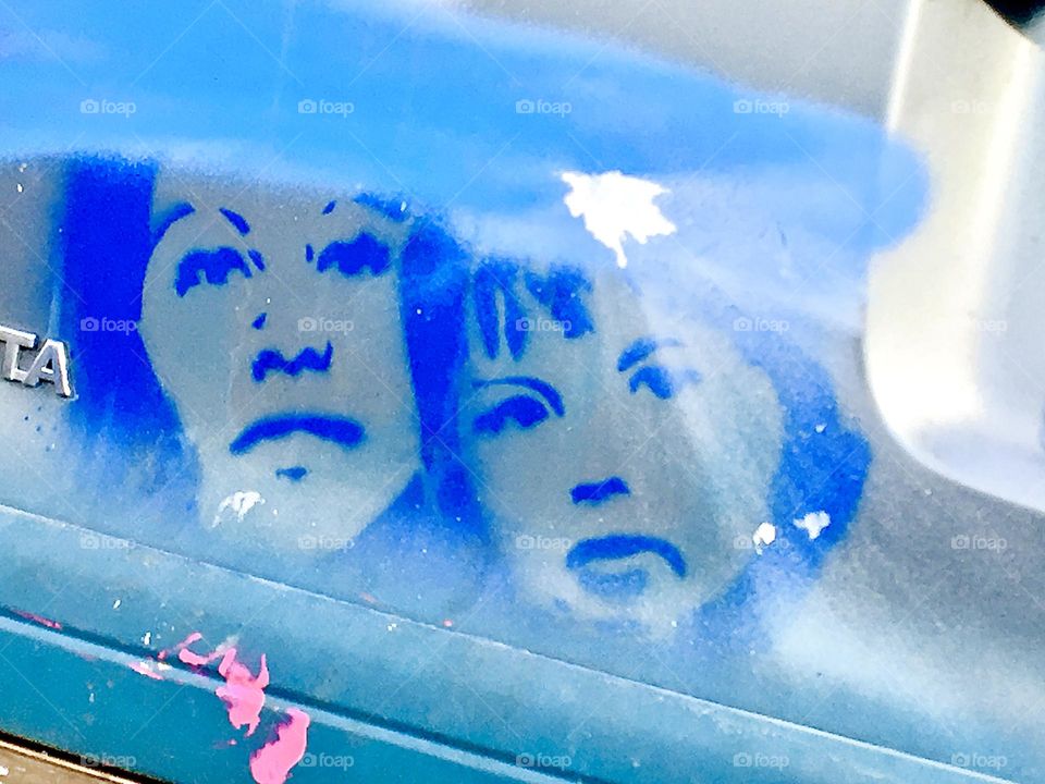 A graphic design sticker of some kind seen through the reflective glass of a car window photographed in 2021. The blue to green color tones add up to a nice composition. Hypnotic Productions