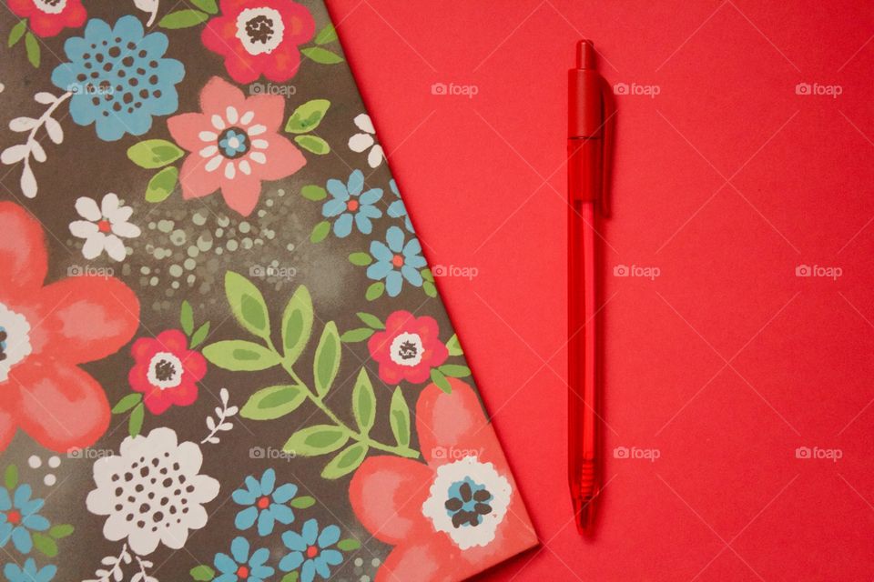 Flat lay of a multi-colored floral binder and red pen on a red background 