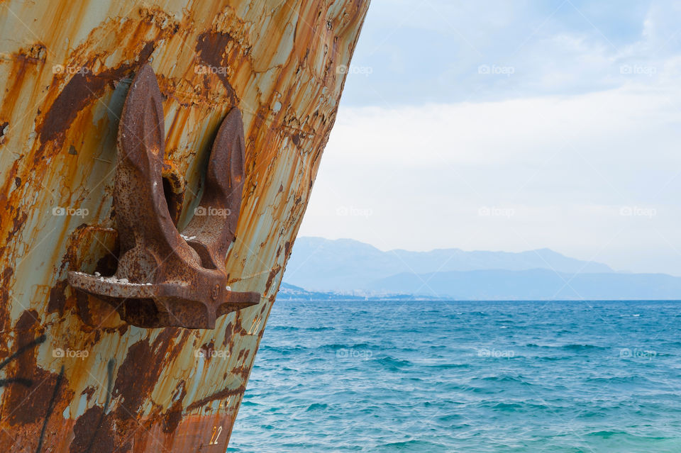 Corroded shipwreck washed ashore. Close-up of ship bow with an anchor.