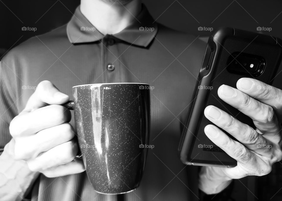 Closeup of a man wearing a polo shirt and drinking coffee while on his cell phone in black and white.