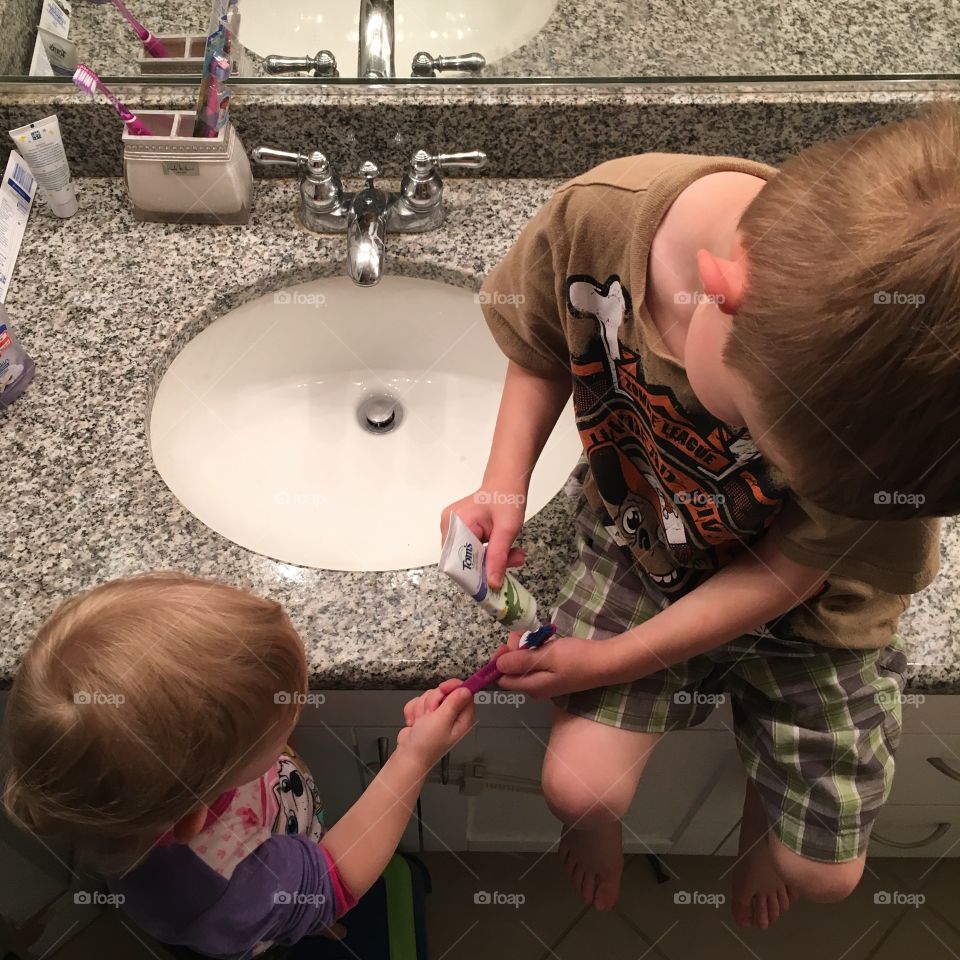 Brother helps sister brush her teeth