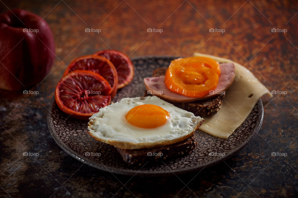 Grain bread with egg, tomato, cheese and bacon on ceramic plate with red orange to desert