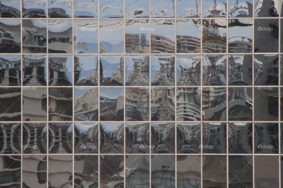 Buildings reflected off the windows of a glass walled building creating a pattern that looks like mosaic tiles. 