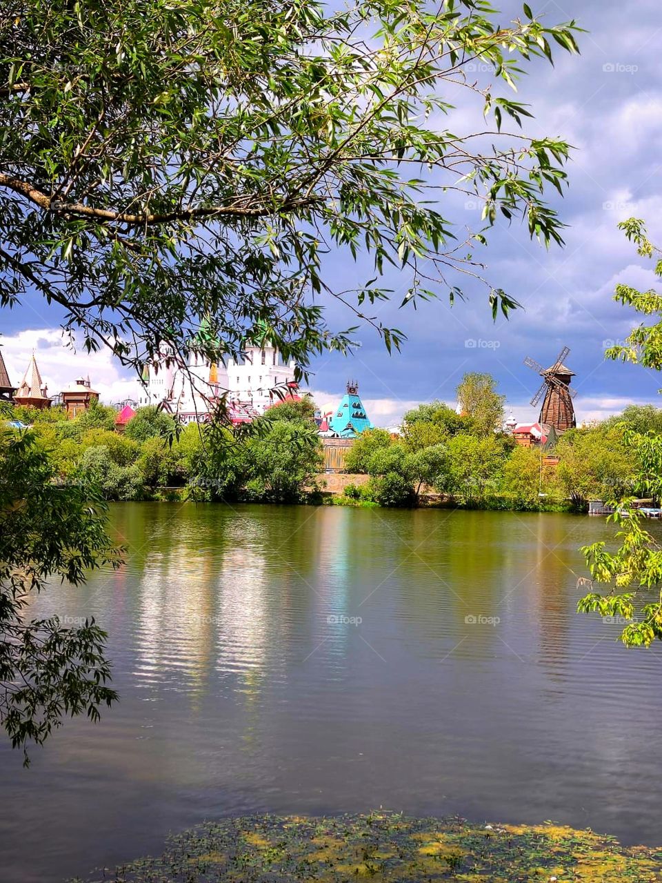 River.  Reflection in the river of trees and domes of towers.  Sunlight shines through the clouds