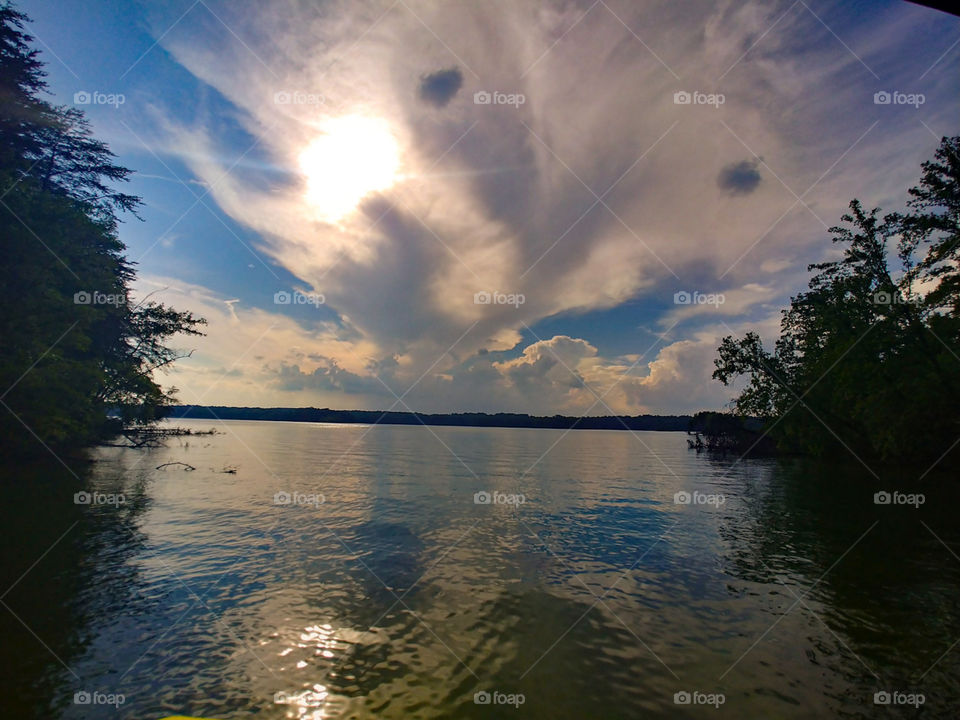 Strange clouds reflecting off of water/lake with sun peeking in behind.