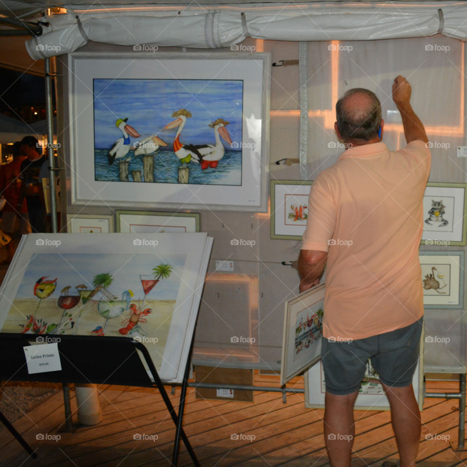 An elderly man arranges his painting for customers to view!