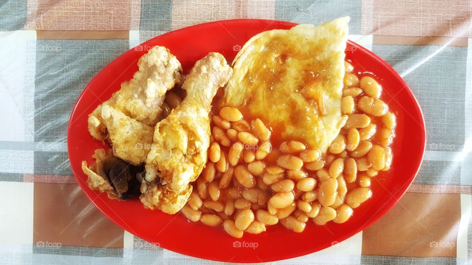Fried drumstick, eggs,  & beans on a red plate