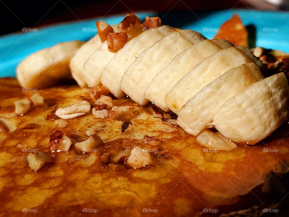 Bannannas slices over buttermilk pancakes with sprinkled nuts and maple syrup