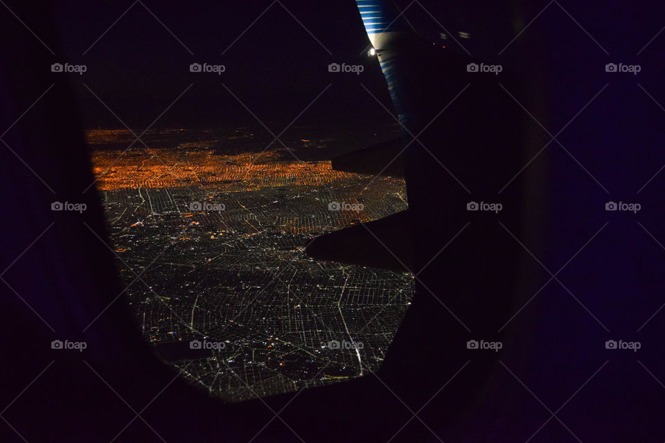 A imagem mostra uma cidade e suas luzes durante a noite, vista da janela de um avião.