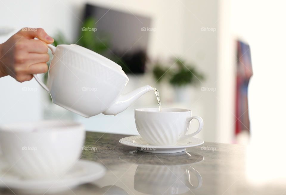 a beautiful white teapot with tea, a girl, her hands in the frame, pours tea into a white cup, natural flower tea