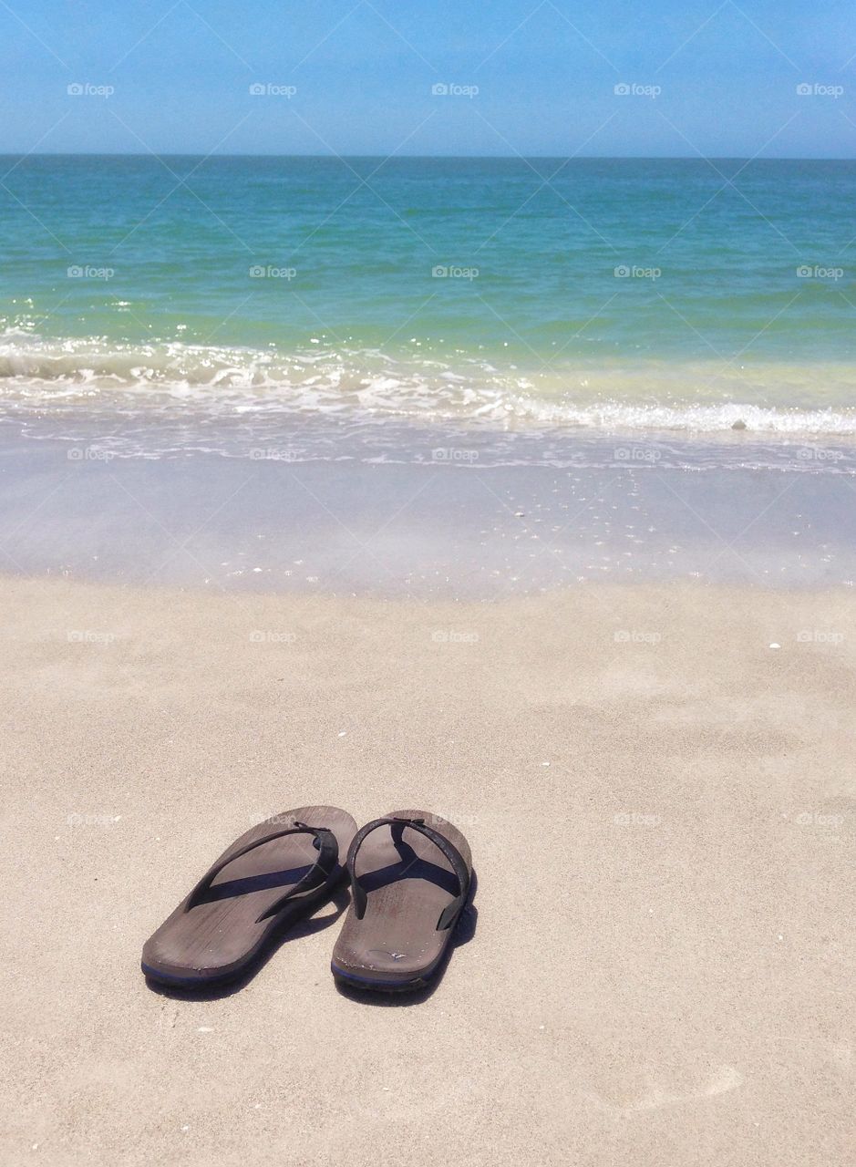 A pair of sandals sit on the beach while it’s owner takes a swim in the calm ocean waves