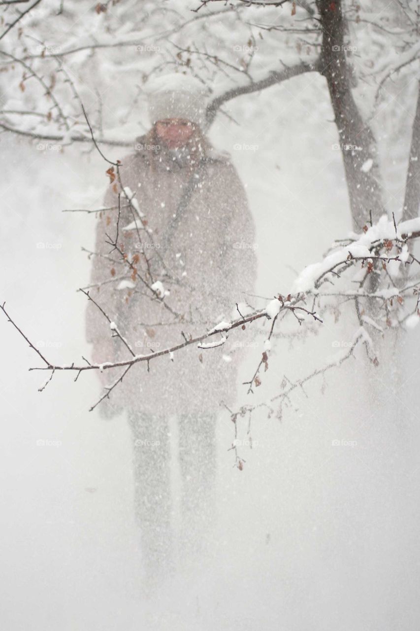 A girl stands under snow falling from a tree