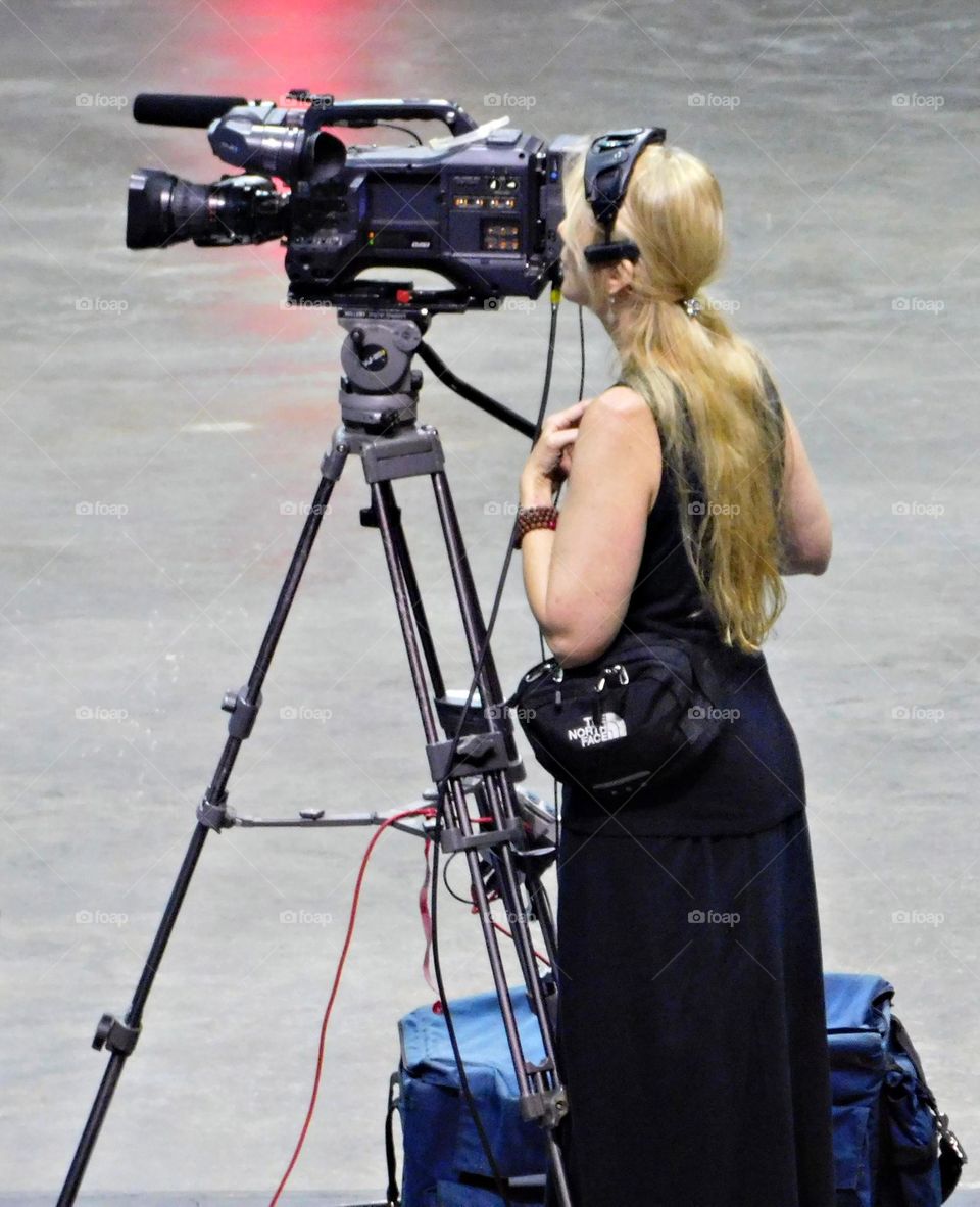 A Video Creator peers through the eye piece of her video equipment during a bishop’s ordinance ceremony 