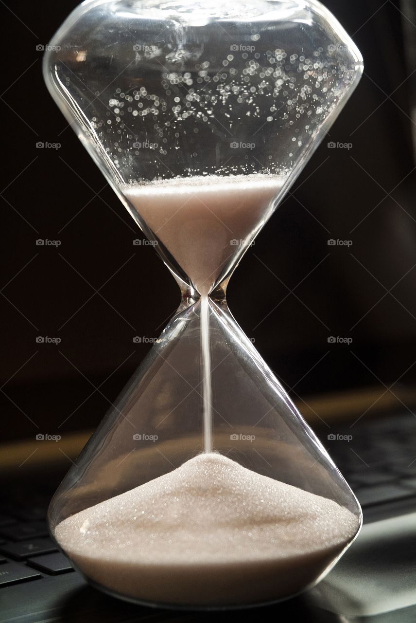 An hourglass sits on the keyboard of a laptop computer.