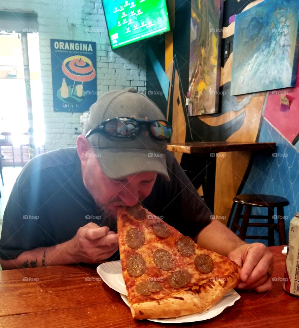 Man eating huge slice of sausage and cheese pizza in vintage, urban location.