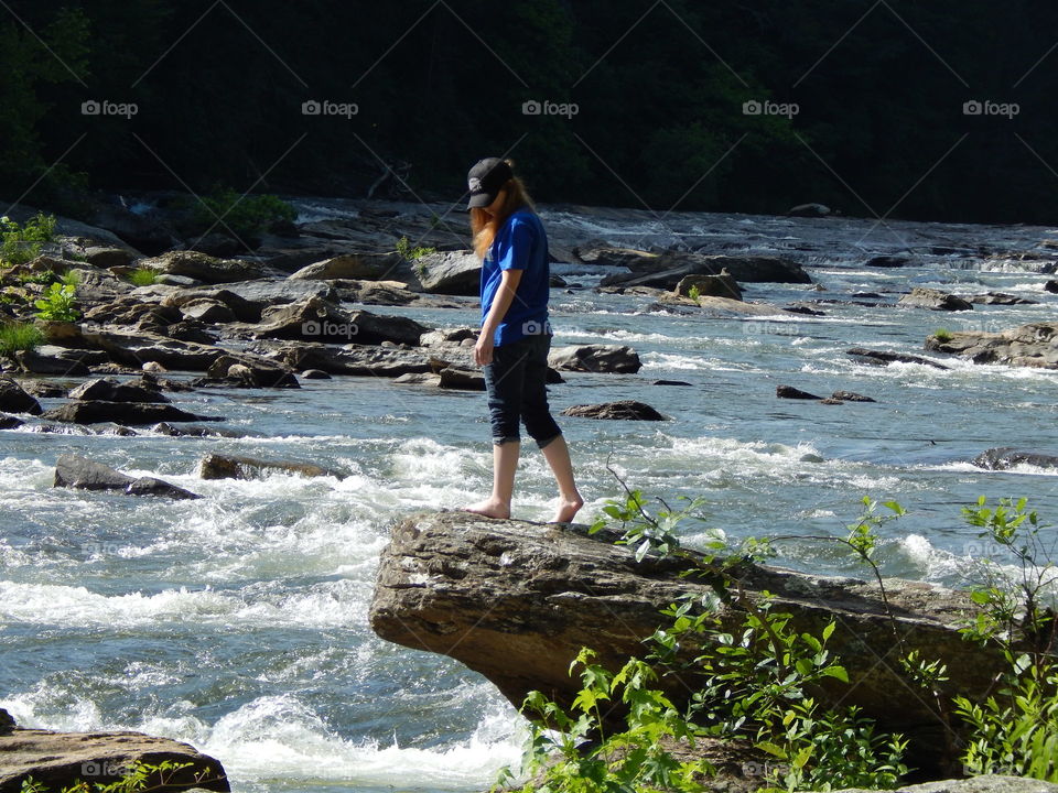 young girl standing on large boulder extending over the Chattooga river.