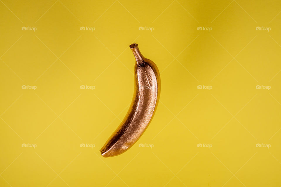 Floating gold banana on yellow background. Minimal food concept