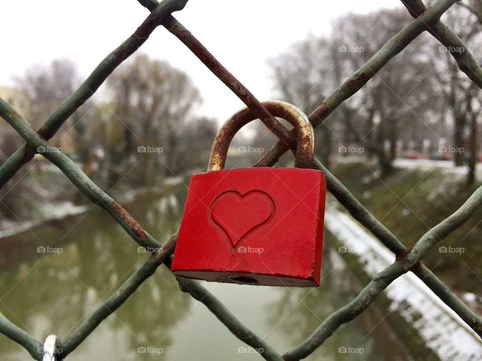 Red padlock with a heart on it hanging on the bridge in winter